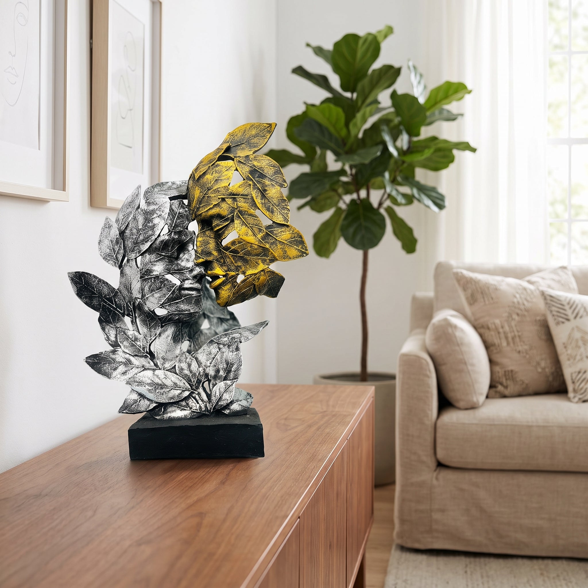 A decorative abstract leaf sculpture in rustic antique finish metallic silver and gold tones on a black rectangular base, displayed on a wooden console table in a bright living room with a sofa and potted plant.