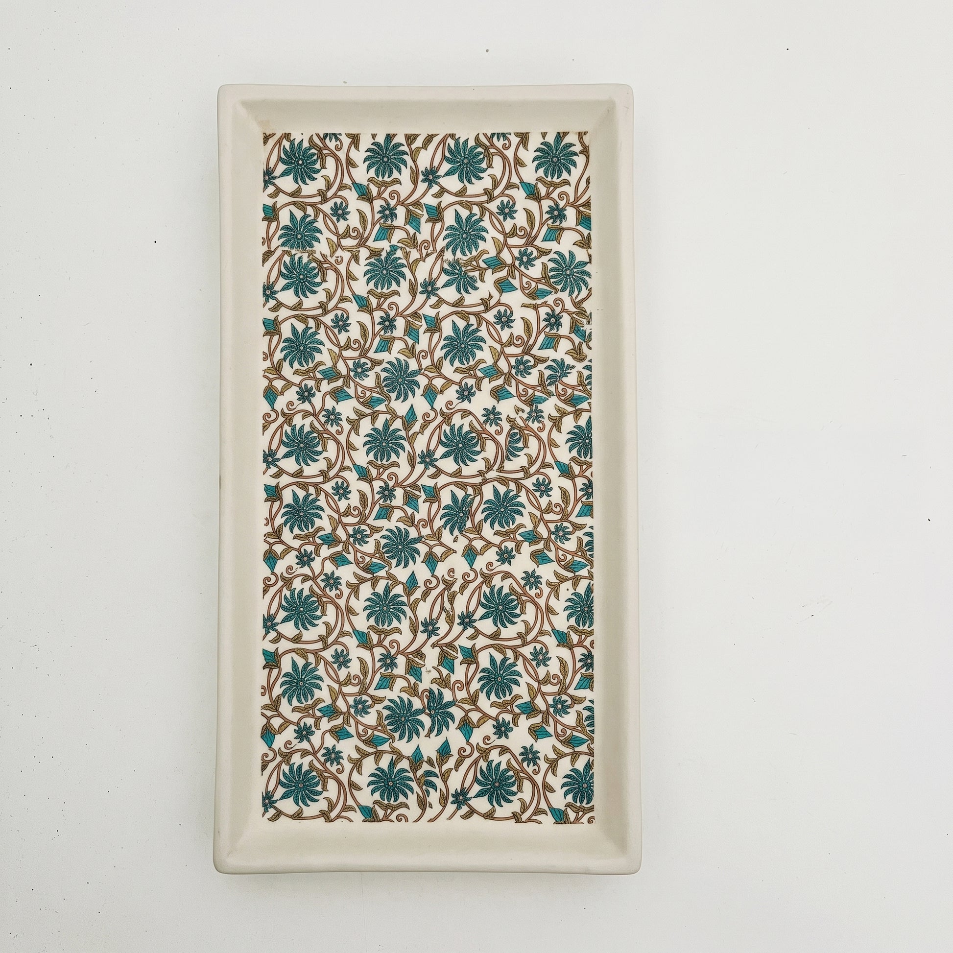 A rectangular ceramic serving tray with a raised rim, featuring a repeating floral pattern in teal and brown on a cream background.