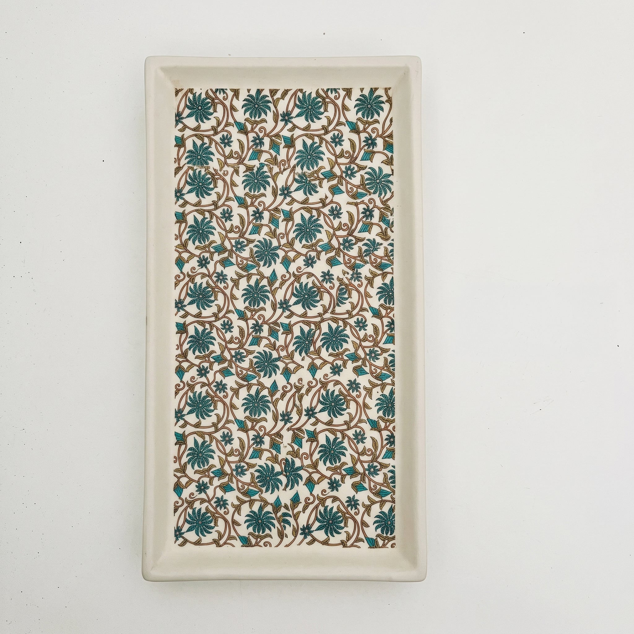 A rectangular ceramic serving tray with a raised rim, featuring a repeating floral pattern in teal and brown on a cream background.