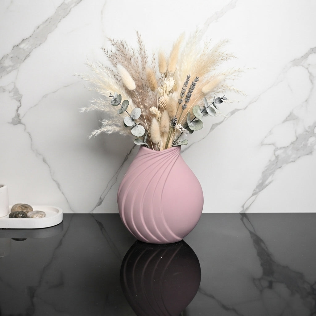 A dusty pink ribbed ceramic vase filled with dried pampas grass and eucalyptus stems, set on a dark marble surface against a white marble wall.