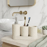 A beige stone-look bathroom organizer set on a marble countertop, including a soap dispenser, toothbrush holder, cup, and tray, with a sink and mirror in the background.